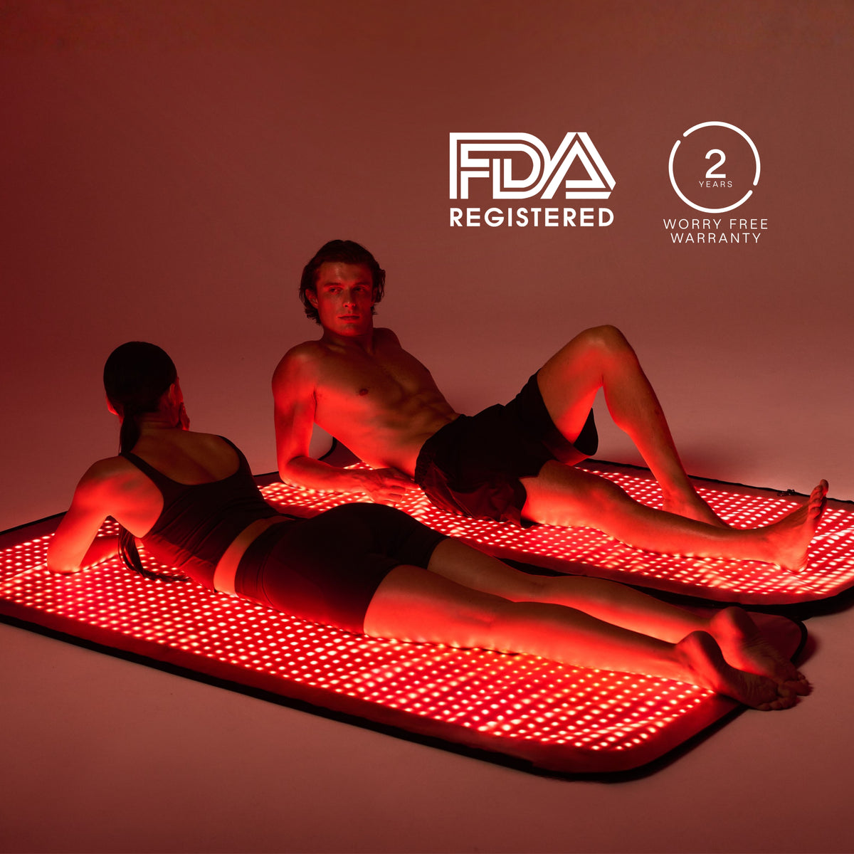 Dos personas reclinadas en esterillas LED Restora+ separadas y encendidas, junto a distintivos de garantía y registro